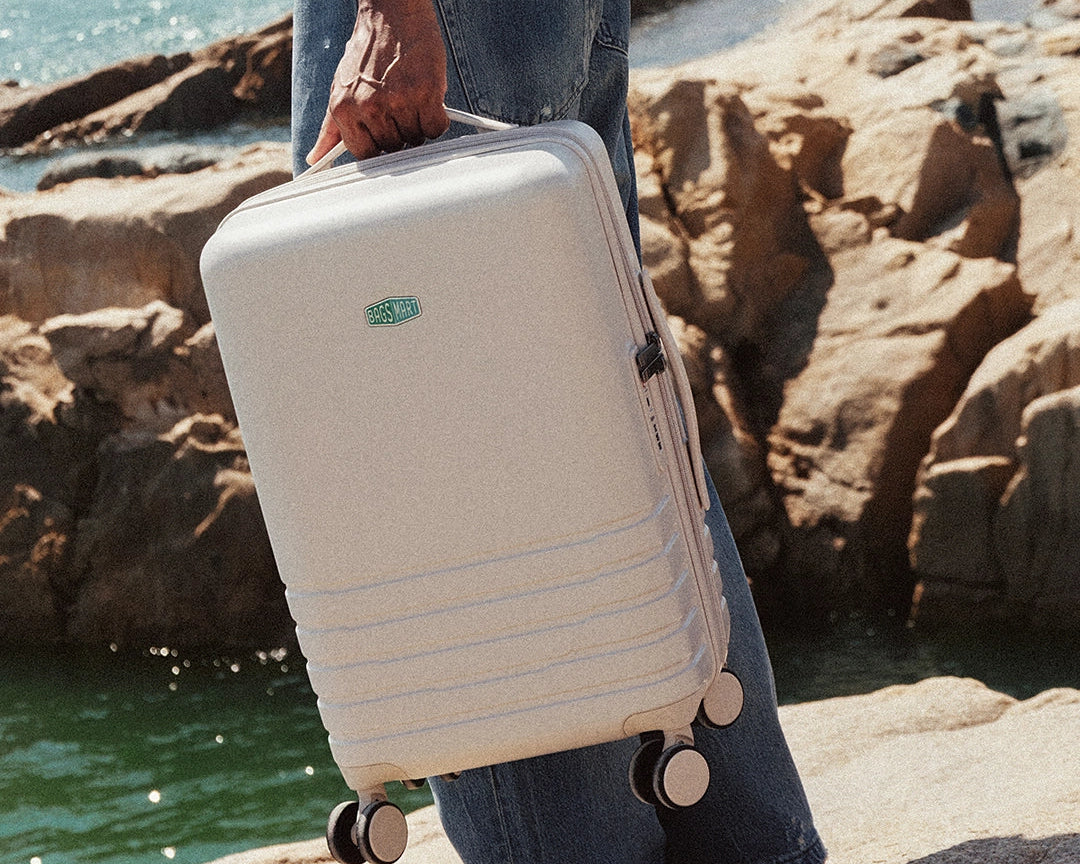Person holding a beige suitcase with a green logo by the sea.
